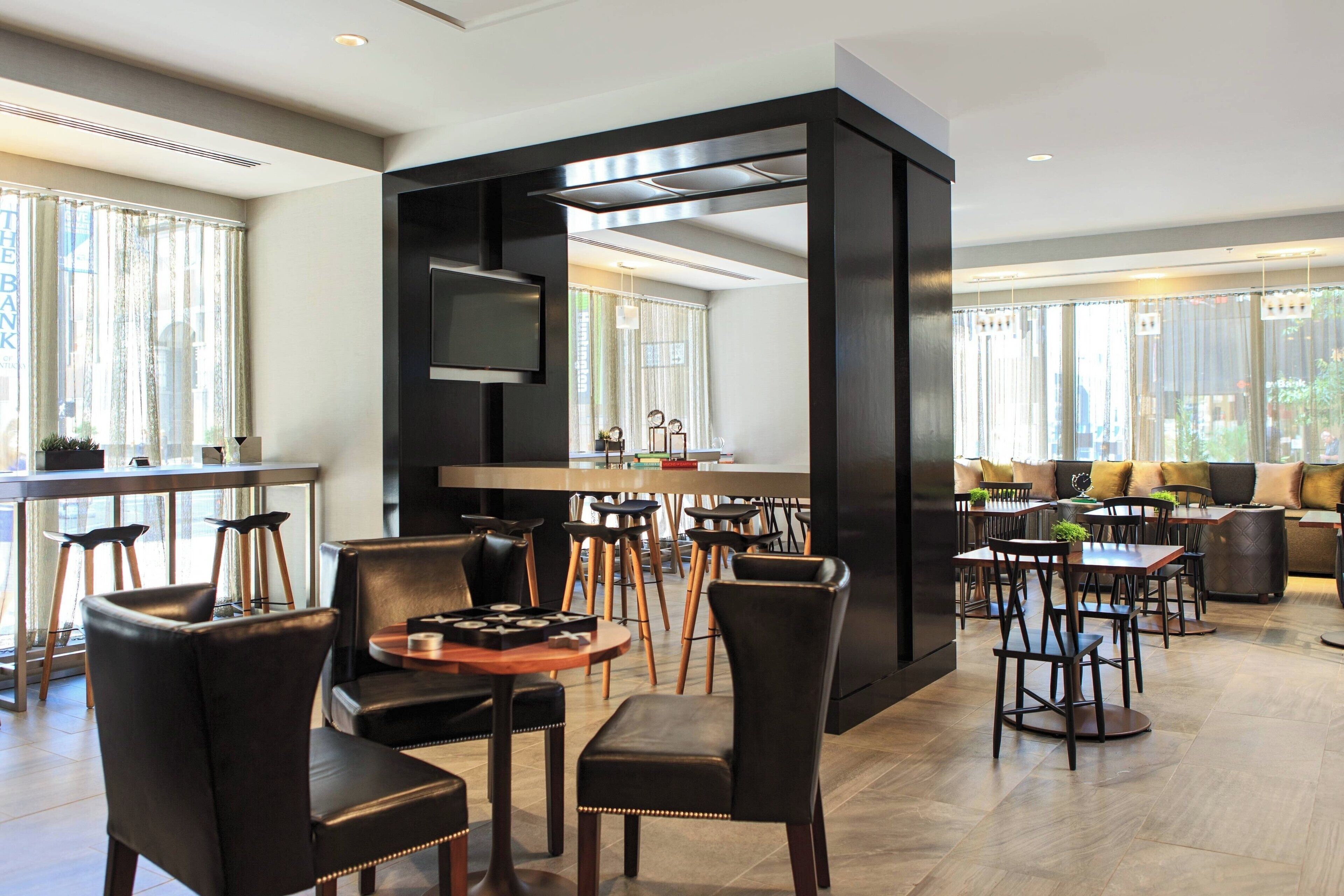 Un espace repas moderne avec des chaises en cuir noir, des tables en bois et un séparateur central de couleur noire.