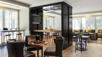 Uma sala de jantar moderna com cadeiras de couro preto, mesas de madeira e um painel preto central.