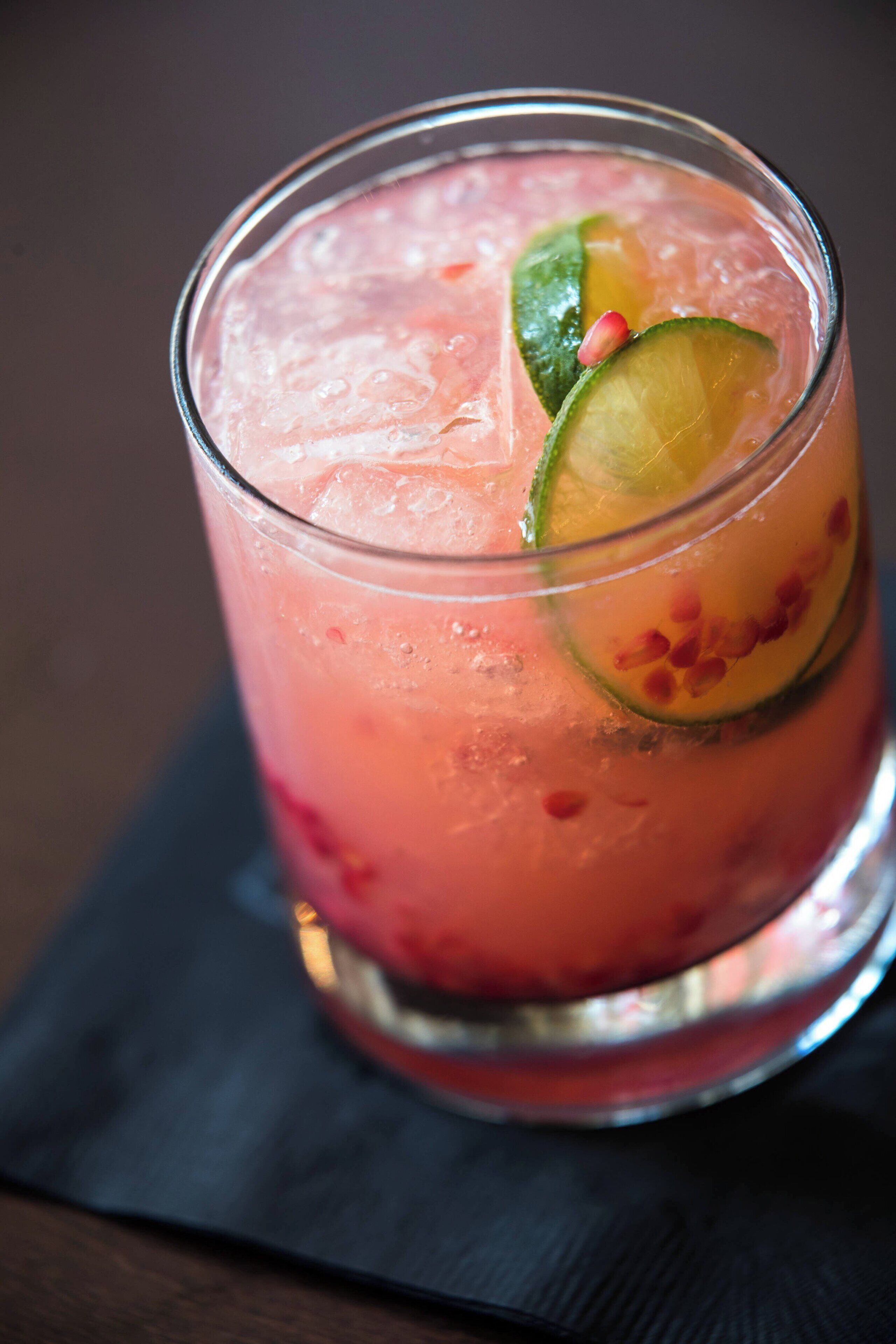 A glass of pink beverage with ice cubes and lime slices.