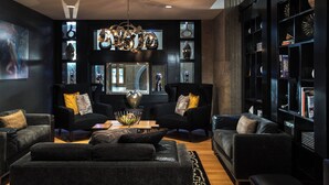 Ein modernes Wohnzimmer mit dunklen Sofas, einem Couchtisch und einer Chandelier. Es gibt Bücherregale mit dekorativen Gegenständen und ein großes Fenster.