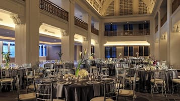 Un salón de baile amplio con varias mesas redondas dispuestas para comer, techos altos con detalles ornamentales y un balcón con vistas al salón.