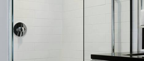 Un baño moderno con paredes de azulejos blancos, cabina de ducha de cristal, lavamanos cromado y un perchero para toallas.