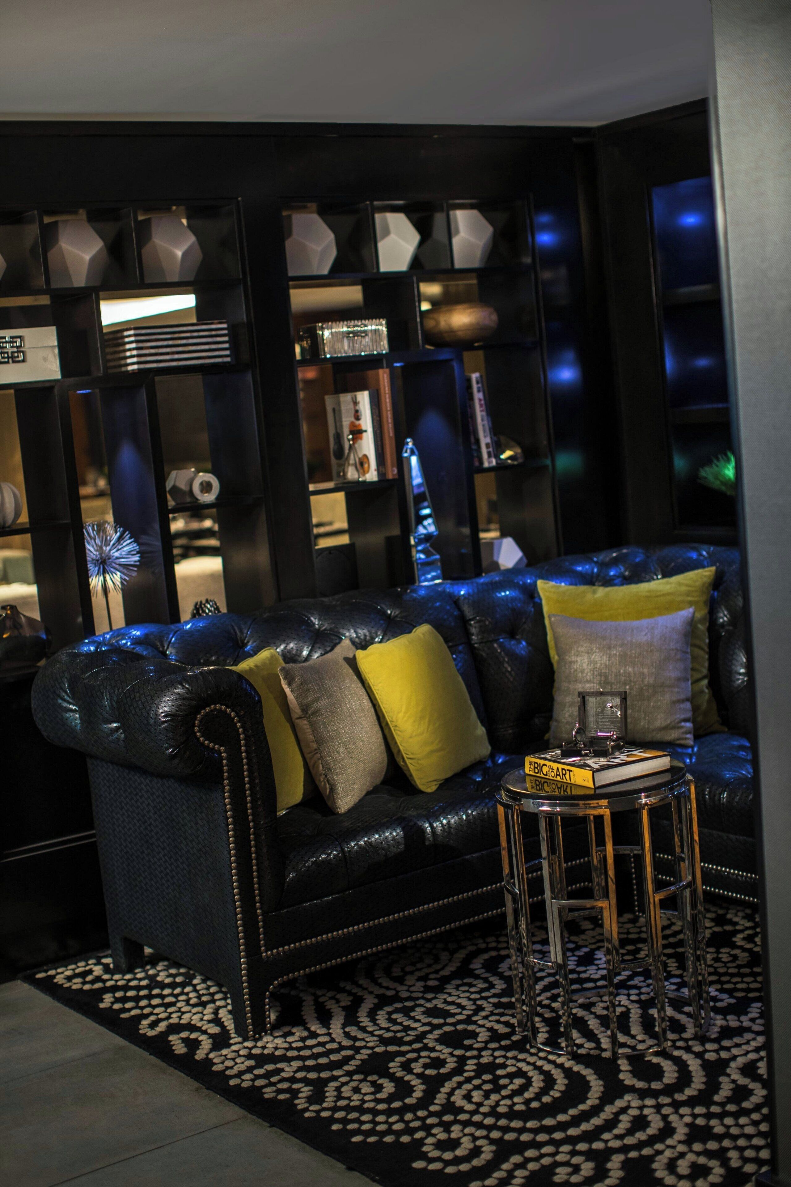A dark-themed living room with a leather sofa, a patterned rug, and a small side table with books.