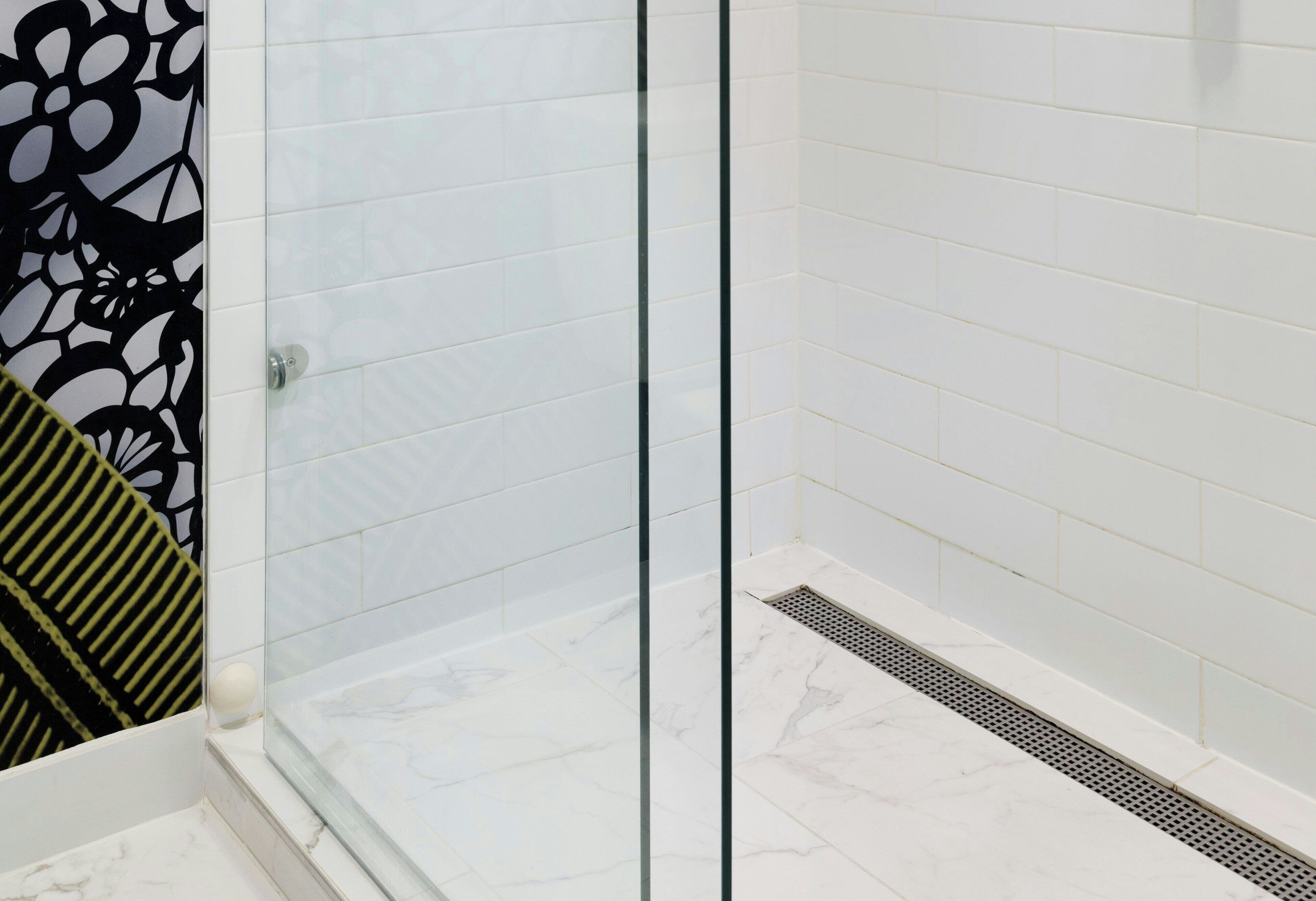 Une salle de bain moderne avec des carreaux blancs, une douche en verre et un motif décoratif noir et vert sur le mur.