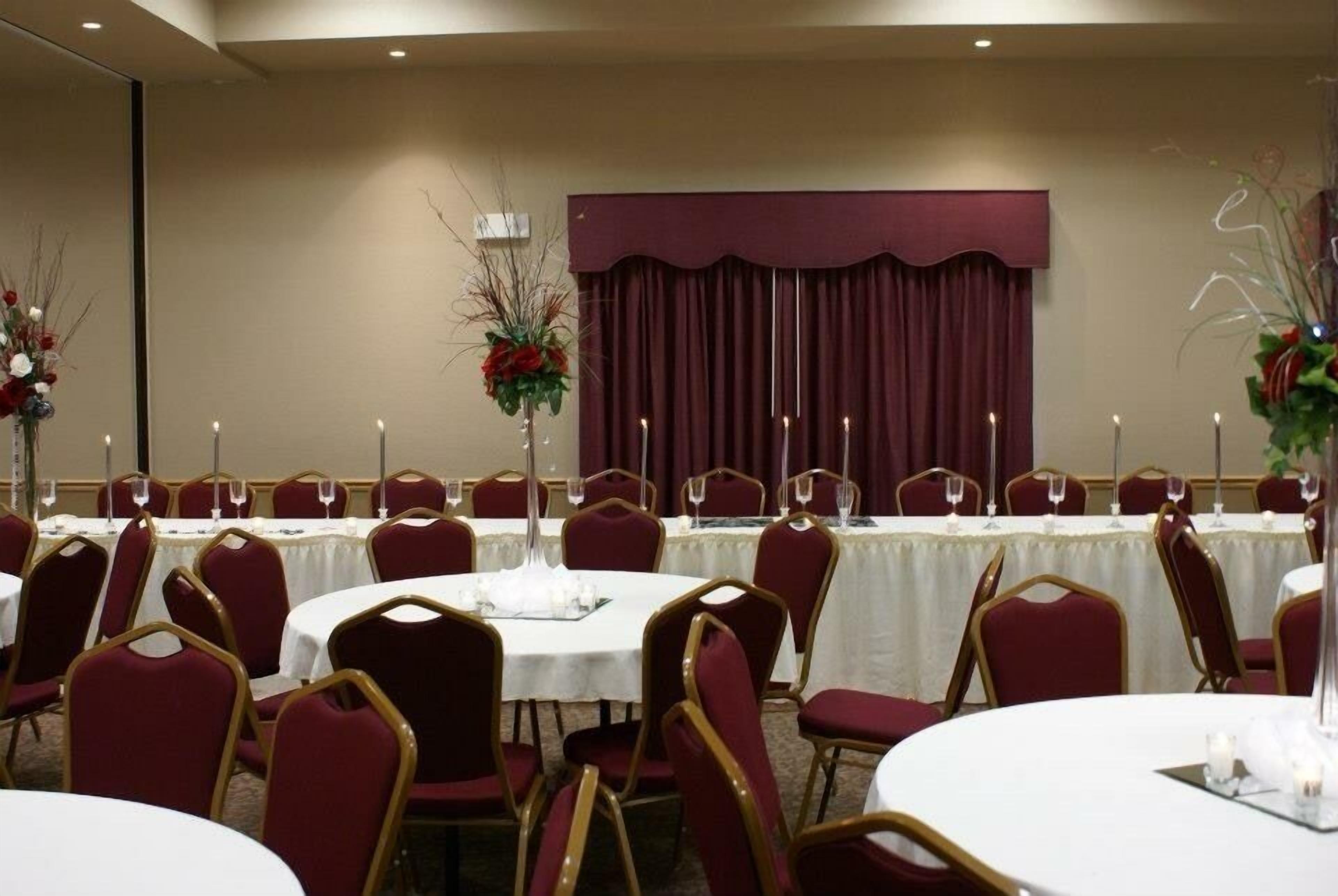 Un salón de banquetes con mesas redondas, sillas rojas y manteles blancos.