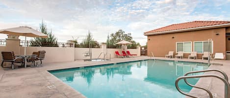 A swimming pool with lounge chairs and umbrellas, surrounded by a building with a tiled roof.