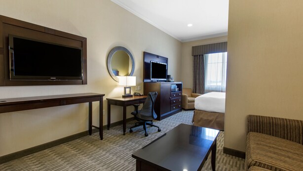 A hotel room with a large flat-screen TV, a desk with a chair, a bed, a sofa, and a large mirror. - The Oaks Hotel Paso Robles (Paso Robles)