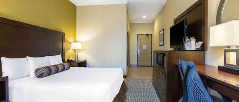 A hotel room with a large bed, a desk with a chair, a television, and a mirror.