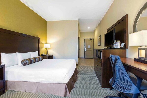 A hotel room with a large bed, a desk with a chair, a television, and a mirror.