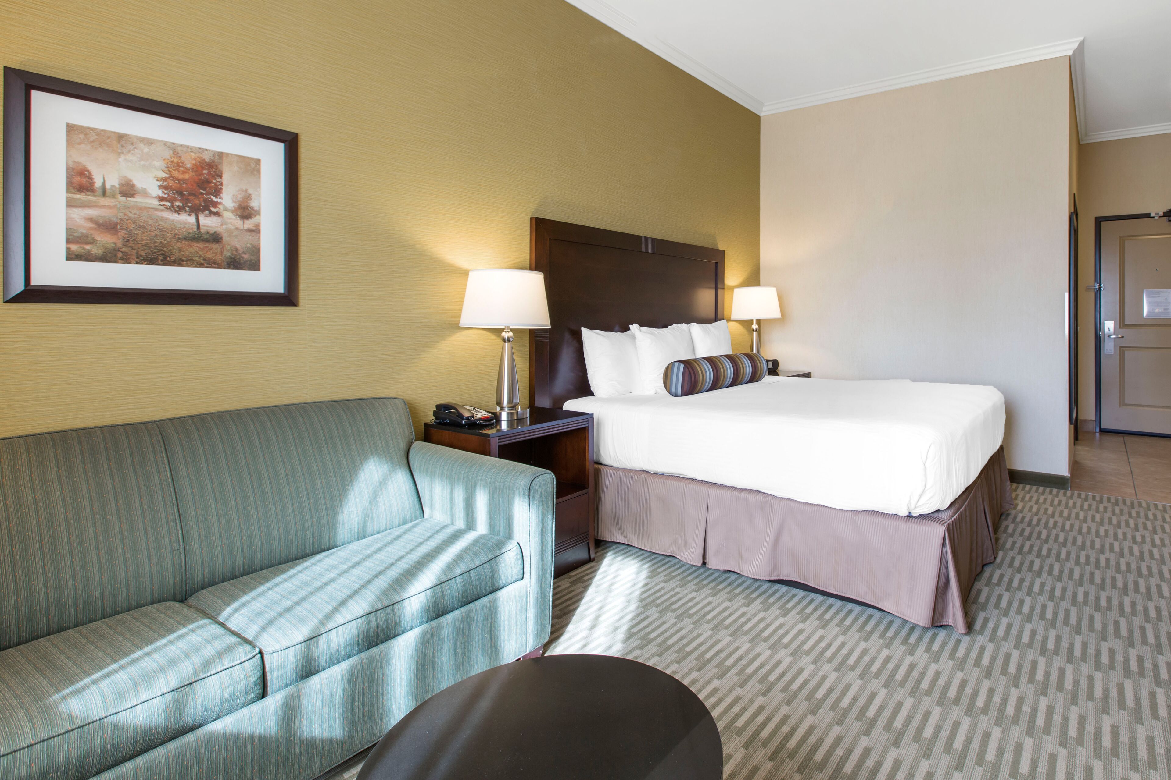 Una habitación de hotel con una cama, un sofá, una mesita de noche y un cuadro enmarcado en la pared.