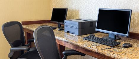 Un espacio de trabajo con dos monitores, una impresora, un teclado y sillas de oficina.