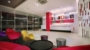 Un espace d’accueil d’hôtel au design moderne, comprenant un comptoir d’accueil, des chaises colorées et une cloison en verre.