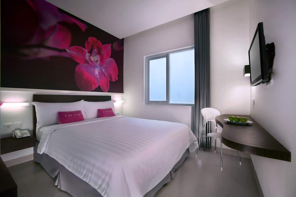 Una habitación de hotel moderna con una cama grande, un escritorio, un televisor de pantalla plana y una ventana con cortinas.