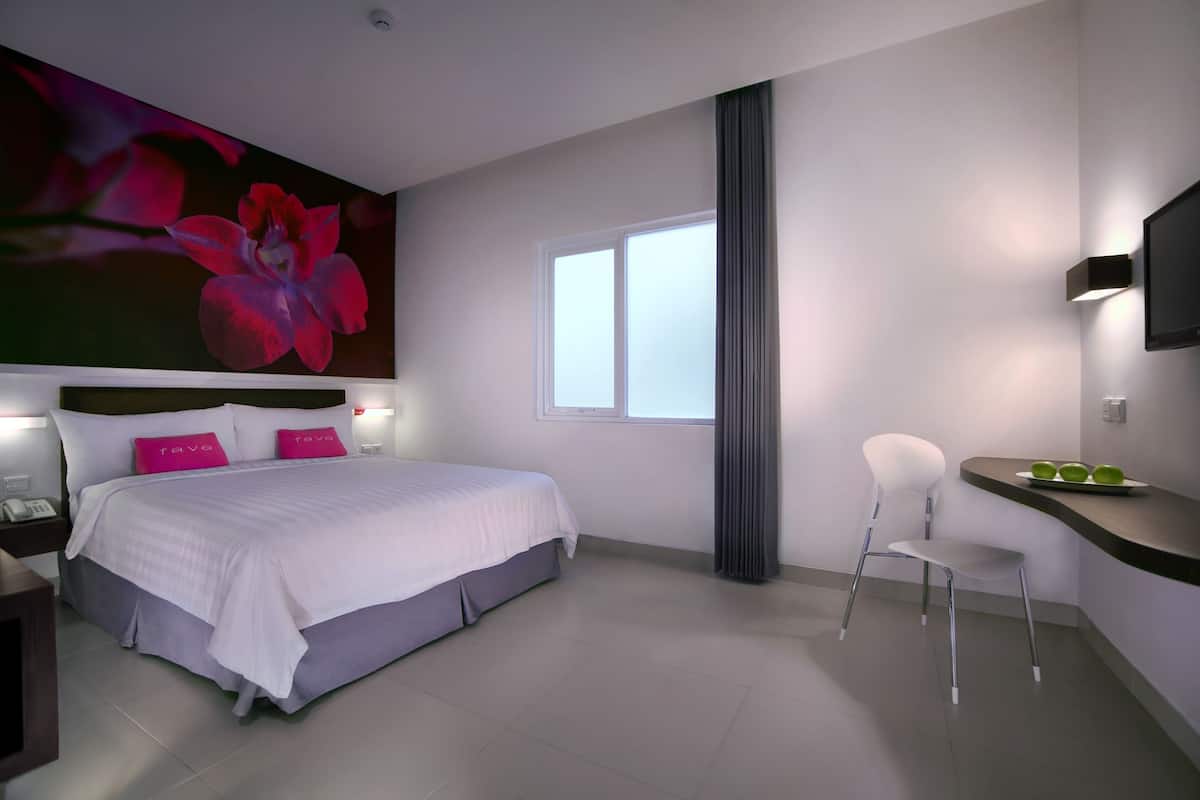 Una habitación de hotel moderna con una cama grande, un escritorio con silla, un televisor de pantalla plana y una ventana con cortinas.