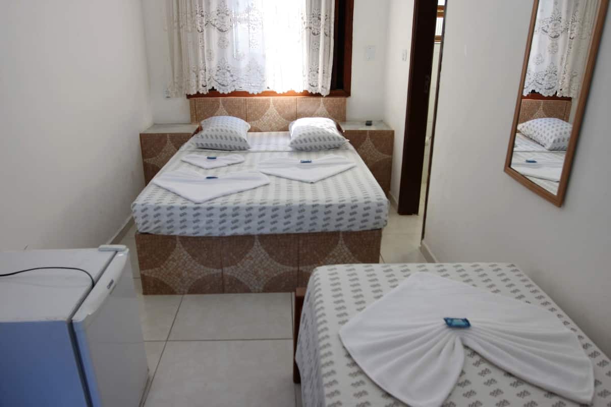 Quarto de hotel com cama, uma mesa pequena, espelho e janela com cortinas.