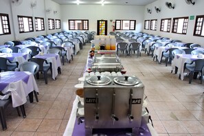 Une cafétéria avec des rangées de tables et de chaises, des distributeurs de boissons et un espace de service central.