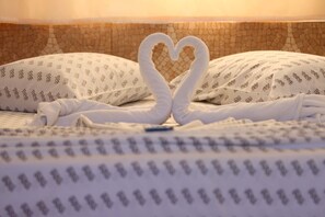 Un lit agrémenté d’une serviette pliée en forme de cœur et de coussins à motifs.