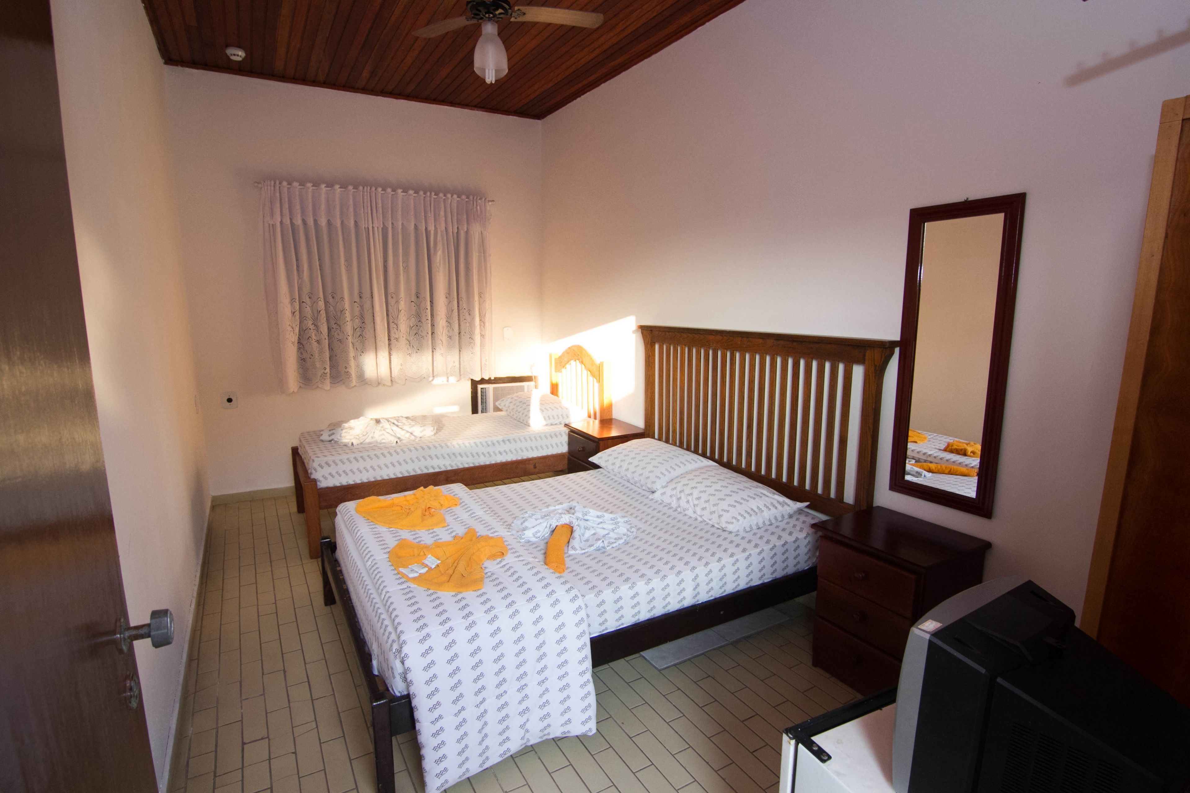 Une chambre avec deux lits, un plafond en bois, un ventilateur de plafond, une table de chevet avec une lampe, un miroir et un téléviseur.