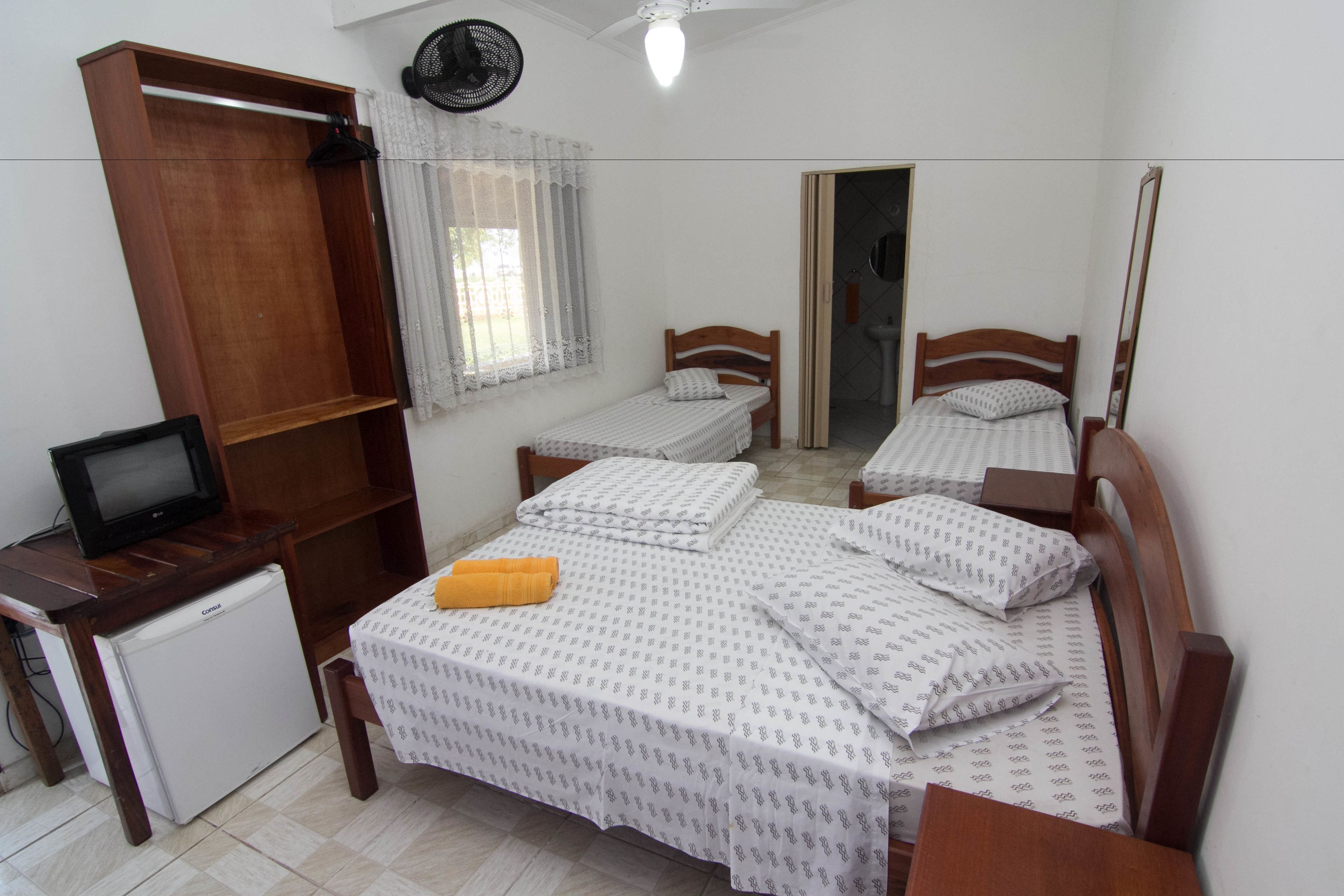 A small, clean room with a single bed, a desk with a computer, and a small refrigerator.