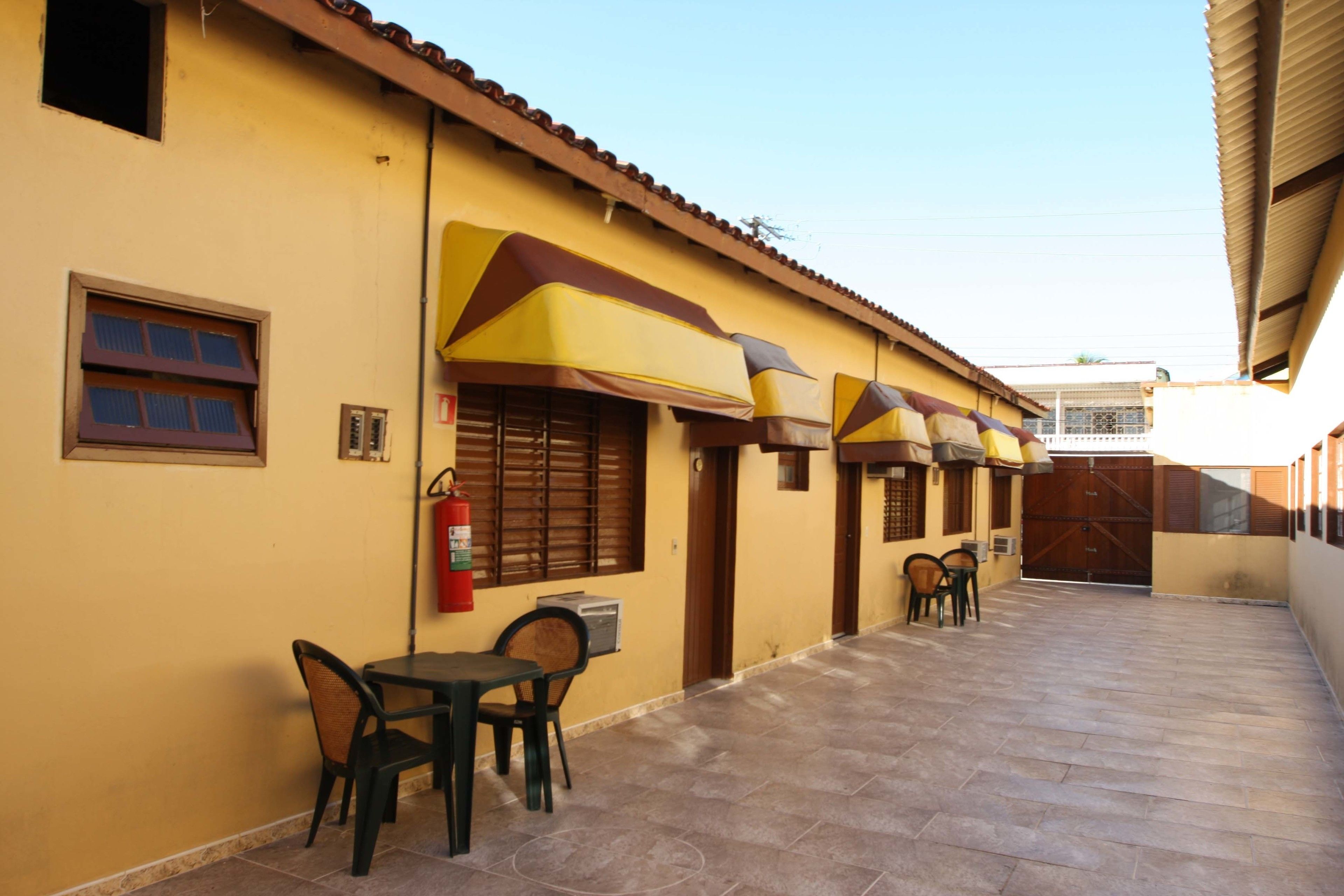 A building with yellow walls and a tiled patio area. There are two tables with chairs, a fire extinguisher, and a door with a window.