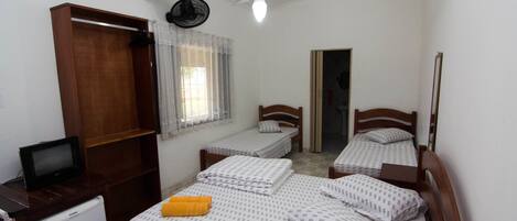 A small, well-lit bedroom with two single beds, a wooden wardrobe, a small desk with a television, and a ceiling fan.