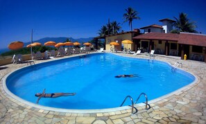 Una piscina con sillas de descanso y sombrillas, rodeada de edificios y palmeras.