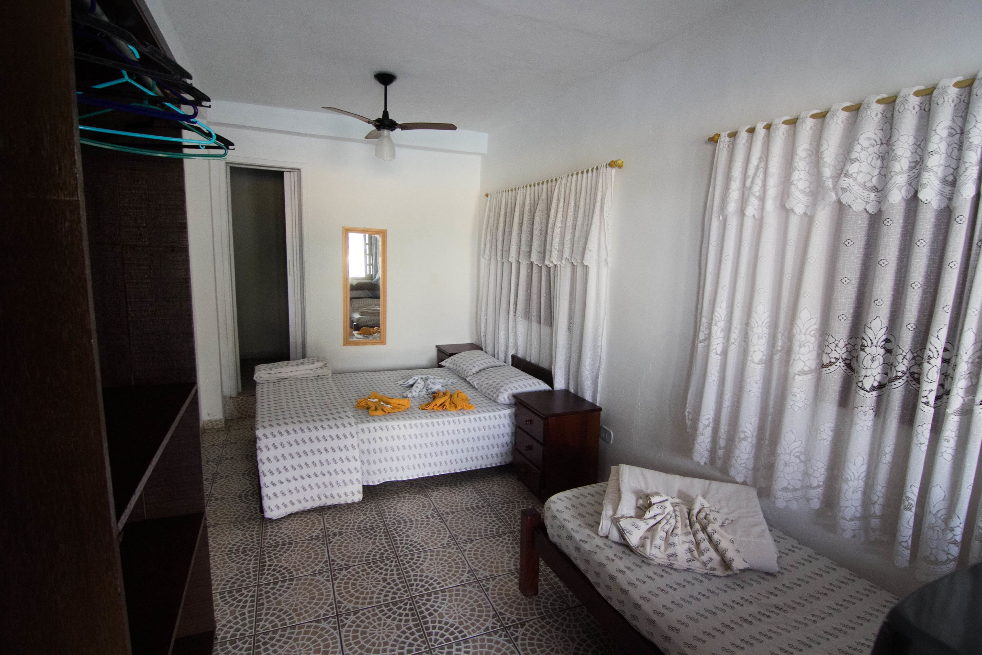A bedroom with two beds, a ceiling fan, a mirror, and patterned curtains.