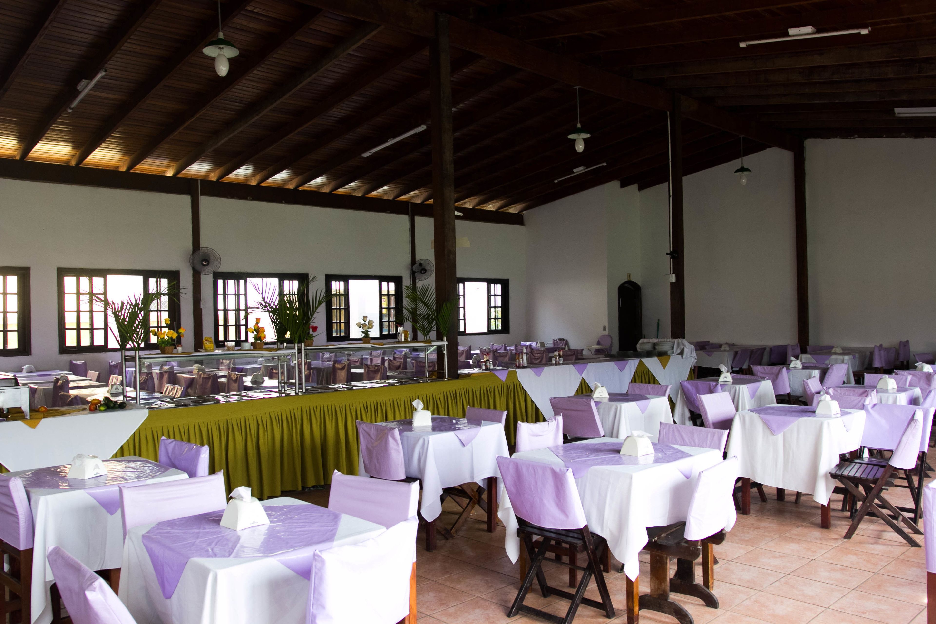 A large dining hall with multiple tables covered in white tablecloths and purple chair covers, arranged in rows.