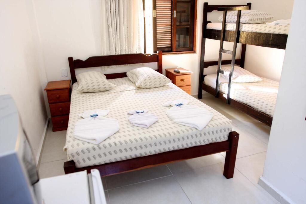 A hotel room with a wooden bed, a nightstand, a bedside table, and a bunk bed.