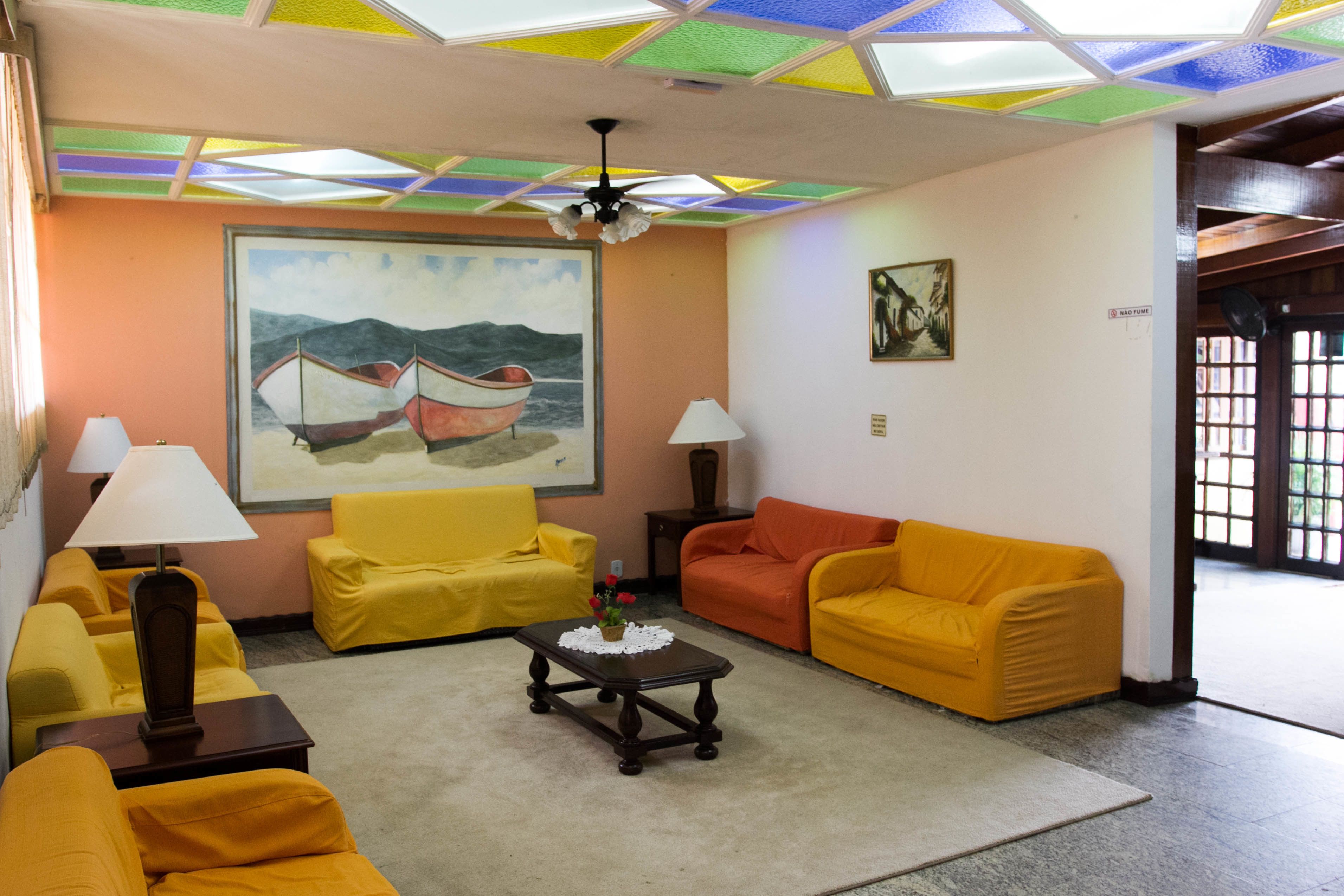 Una sala de estar con sofás amarillos, una mesa de centro, un techo con paneles de colores y obras de arte en las paredes.