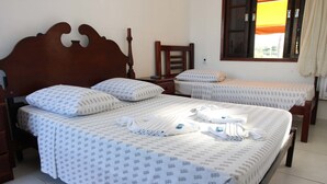 Ein Hotelzimmer mit einem großen Bett, zwei kleineren Betten, hölzernen Kopfteilen und einem Fenster mit einem orangefarbenen Vorhang.