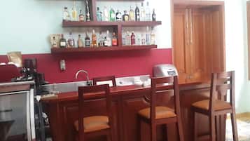 A kitchen with a bar area, wooden chairs, a coffee machine, and a variety of bottles on shelves.
