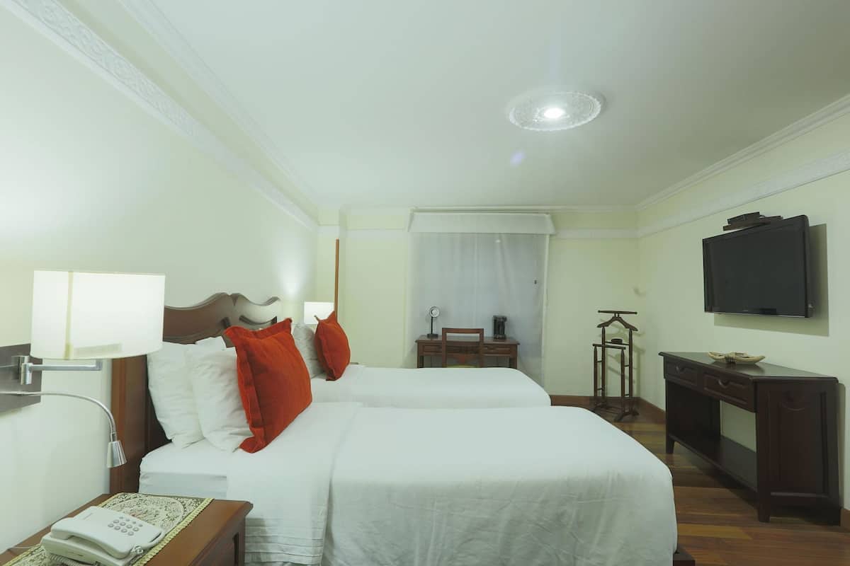 Ein Hotelzimmer mit zwei Betten, einem Schreibtisch, einem Stuhl, einem Telefon, einem Fernseher und einer Deckenleuchte.