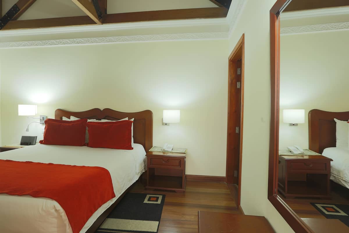 Ein Hotelzimmer mit Bett, Nachttischen, Lampen, einem Spiegel und Holzboden.