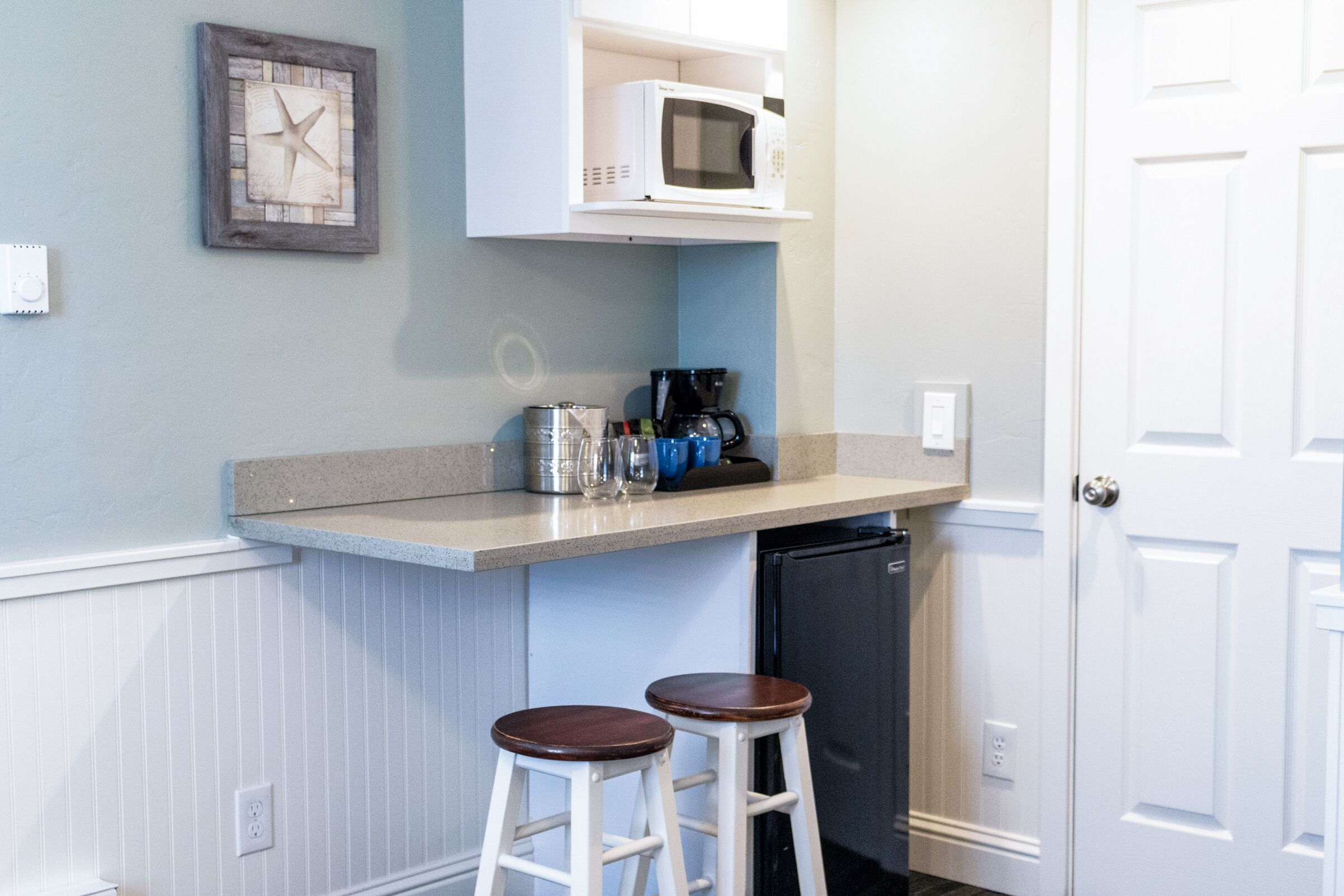 A kitchen with a microwave, coffee maker, and two stools.