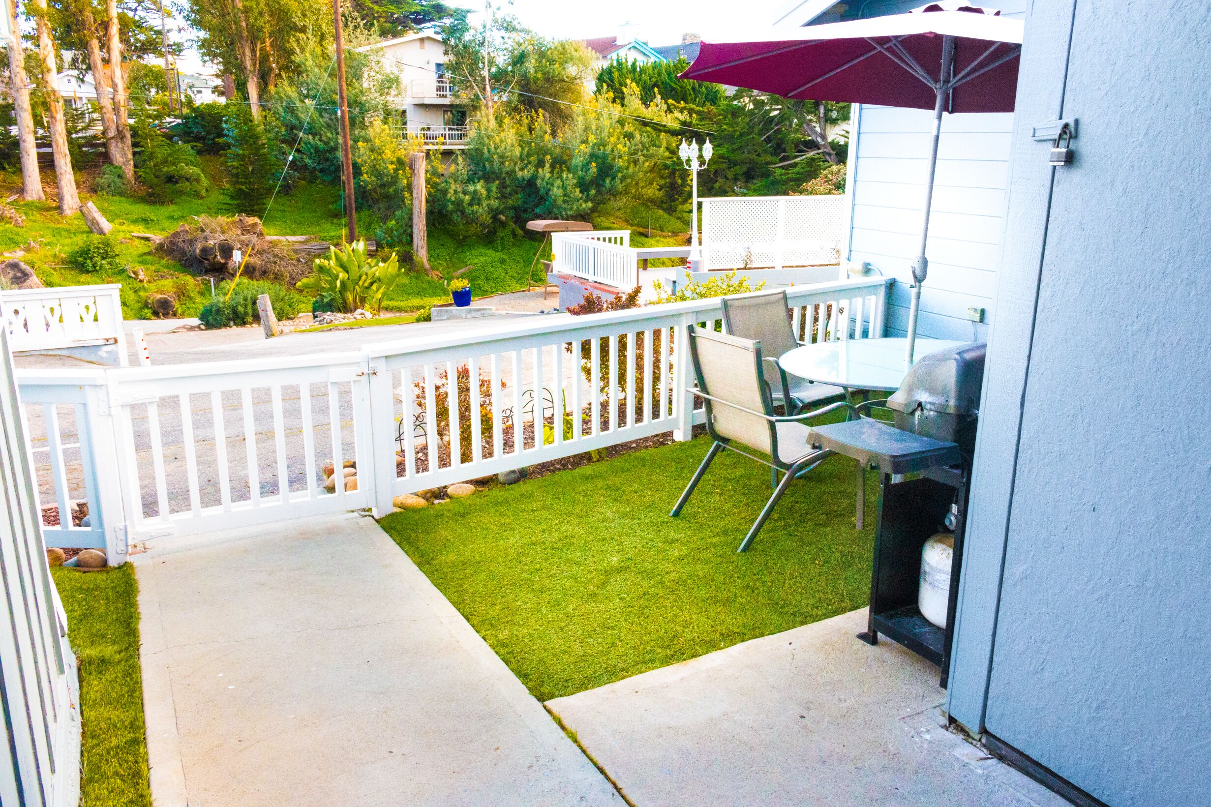 A patio with a grill, outdoor seating, and a white fence.