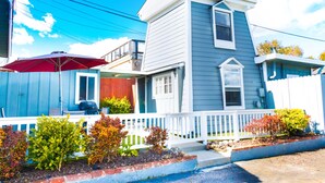 A two-story house with a white porch, a red umbrella, and a small garden with various shrubs. - Ocean Echo Inn and Beach Cottages (Santa Cruz)