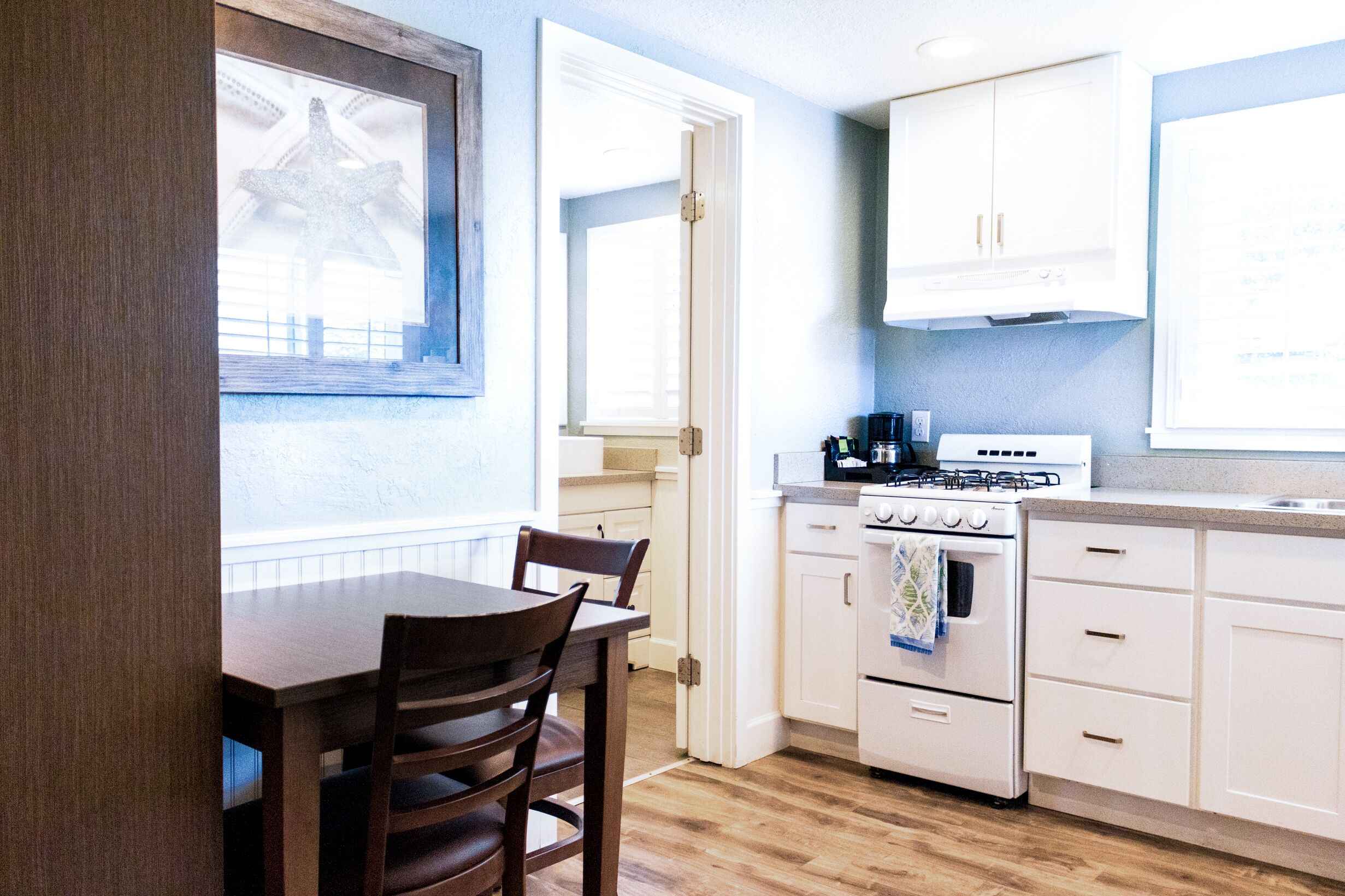 Una cocina con armarios blancos, una estufa y una mesa de comedor con sillas.