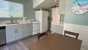 A modern kitchen with white cabinets, a sink, and a stove. There is a dining table with chairs and a clock on the wall. - Ocean Echo Inn and Beach Cottages (Santa Cruz)
