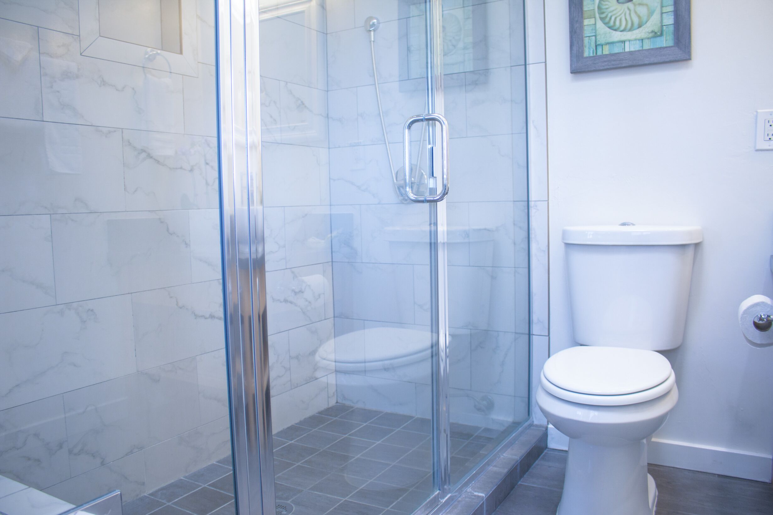 A bathroom with a glass shower enclosure, a white toilet, and a marble-tiled wall.