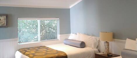 A room with two beds, a window with blinds, a lamp, and a ceiling with recessed lighting.