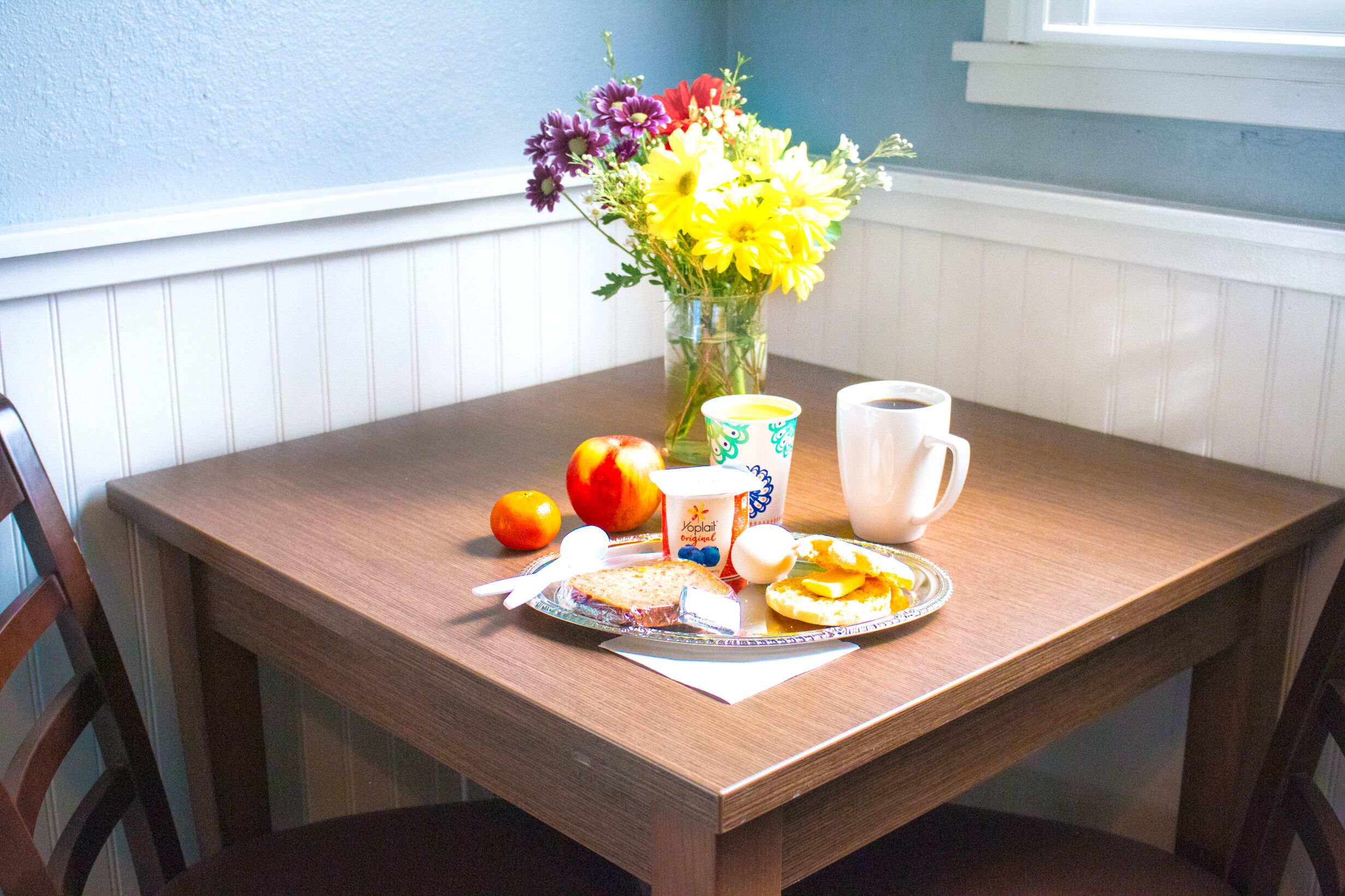 A wooden dining table with a floral arrangement, a plate of food, a cup, and a bowl.