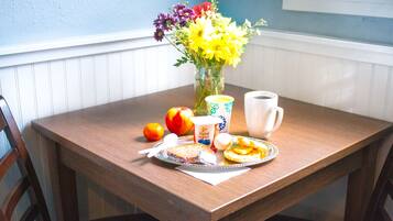 A wooden dining table with a floral arrangement, a plate of food, a cup, and a bowl.