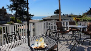 An outdoor patio with a table set for two, a white fence, and a view of the ocean. - Ocean Echo Inn and Beach Cottages (Santa Cruz)