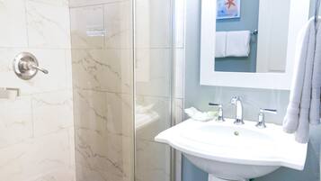 Une salle de bain avec une douche à parois de verre, un lavabo blanc et un miroir.
