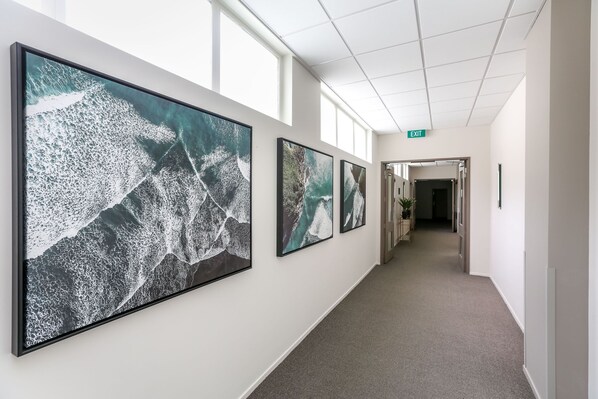 Un couloir aux murs ornés de grandes peintures abstraites, doté d’un sol recouvert de moquette et d’un panneau indiquant la sortie.