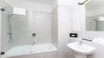 A modern bathroom with a glass-enclosed shower, a white bathtub, and a sink with toiletries.