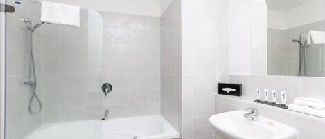 Un baño moderno con ducha de vidrio, una bañera blanca y un lavabo con artículos de aseo.