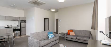 A modern living room with a grey sofa, a dining table, and a kitchen area with a microwave and refrigerator.