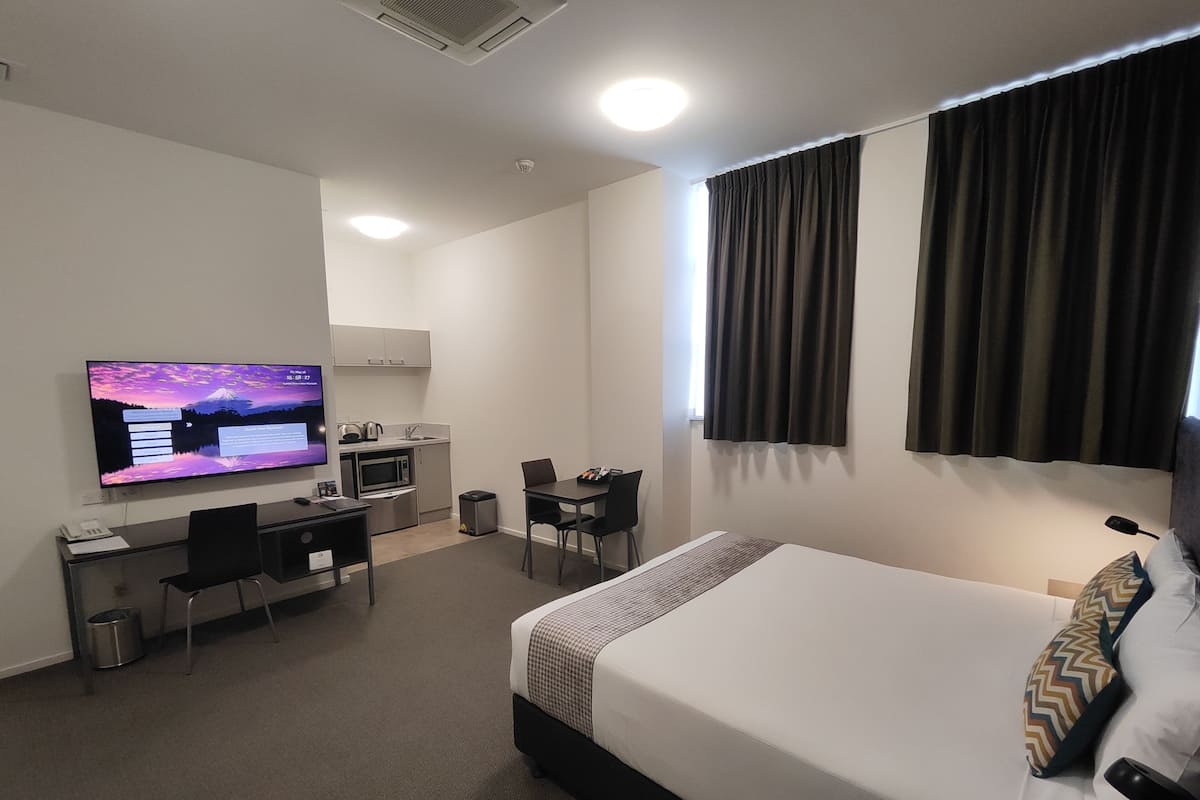 A hotel room with a bed, a desk with a computer, a television, a microwave, and a small kitchenette.